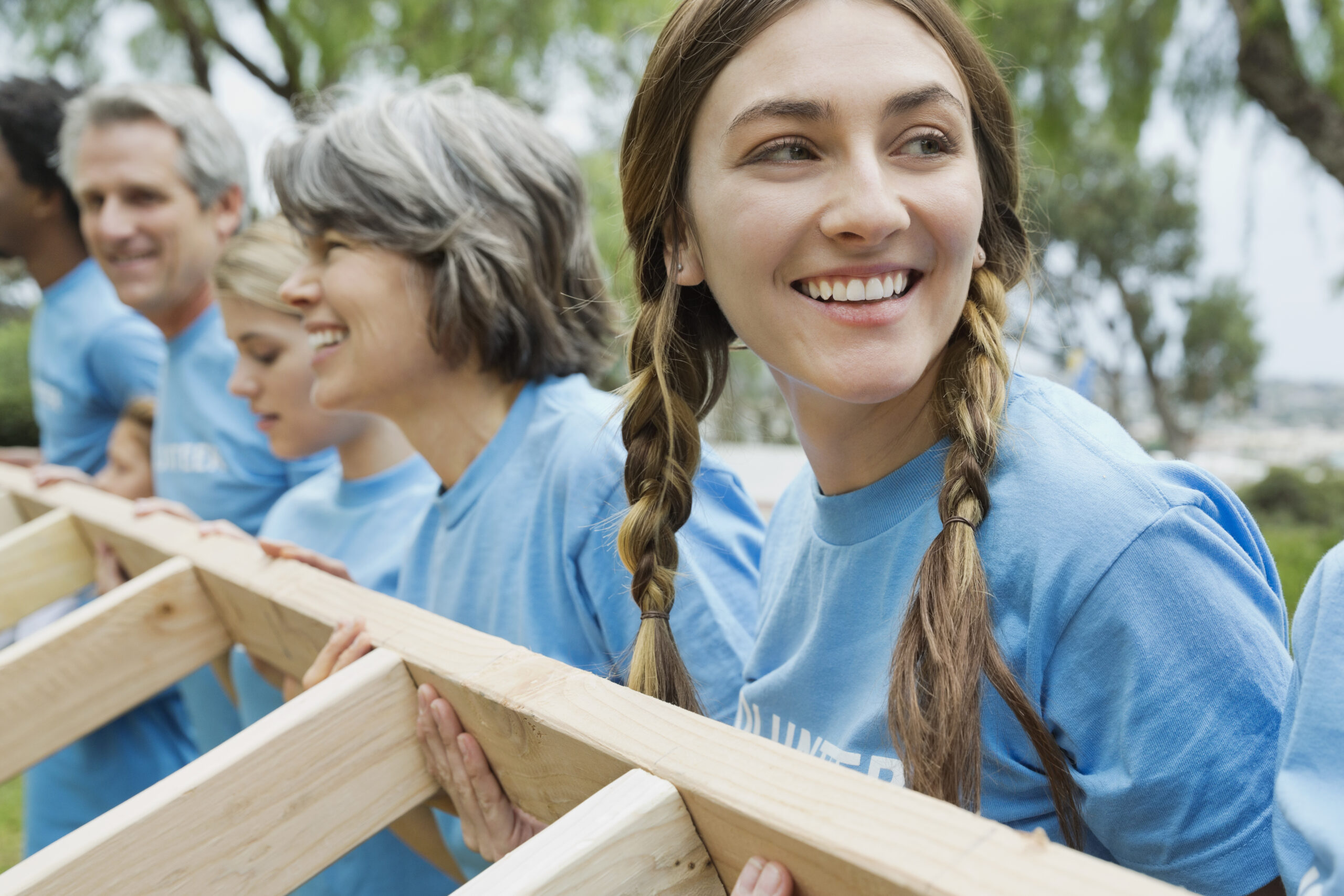 Young woman looking away while lifting wooden frame with volunteers